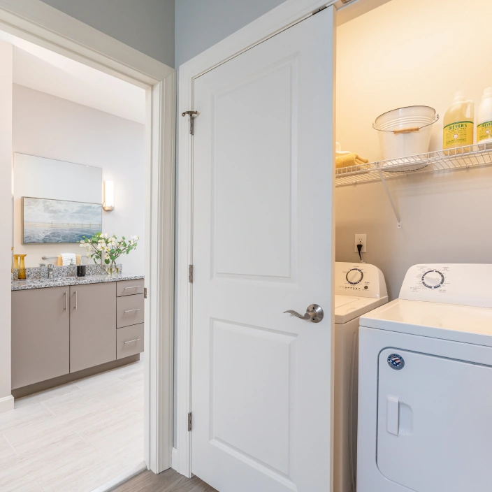 Compact laundry area with washer dryer and shelving beside modern granite bathroom vanity