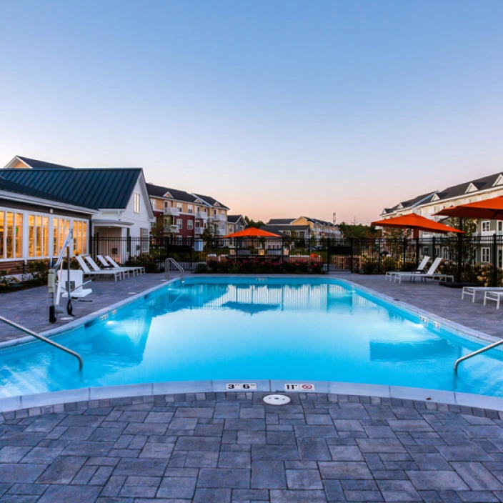 Resort-style swimming pool at luxury apartments with lounge chairs and umbrellas during sunset
