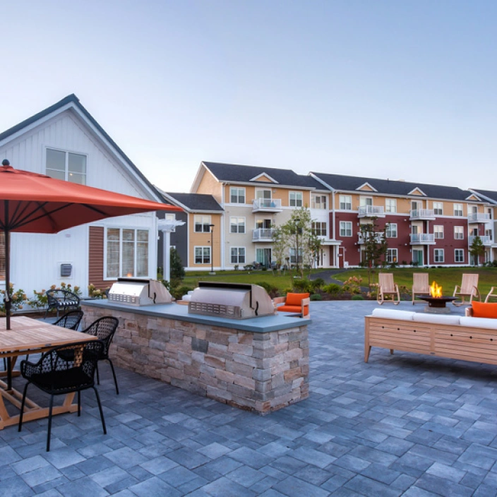 Outdoor grilling area with modern barbecue stations, patio seating, and apartment buildings in background