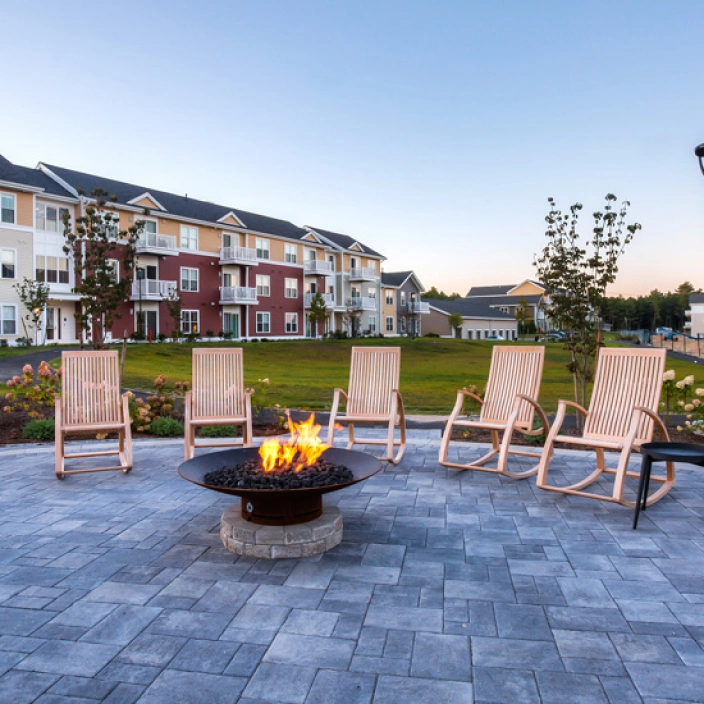 Outdoor fire pit surrounded by wooden rocking chairs overlooking landscaped apartment courtyard