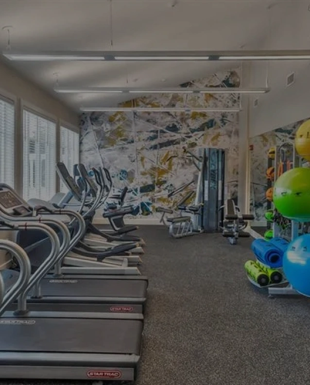 Bright fitness center with treadmills, ellipticals, and weights beneath a vaulted wooden ceiling