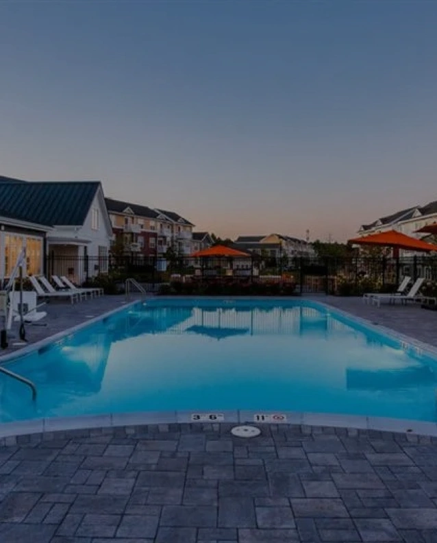 Sparkling blue outdoor pool surrounded by lounge chairs and shaded by tall leafy trees