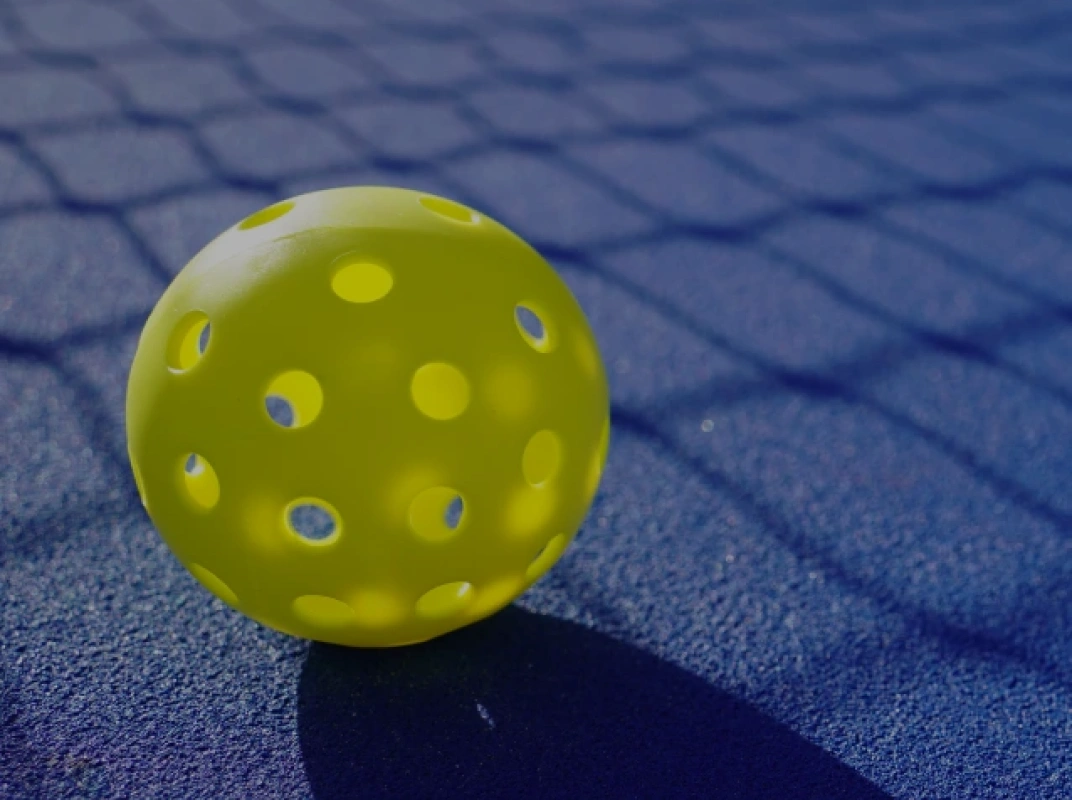 Close-up of a bright yellow-green pickleball resting on a blue outdoor court surface