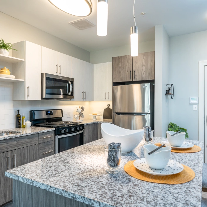 Modern apartment kitchen with granite island, pendant lighting, and stainless steel appliances