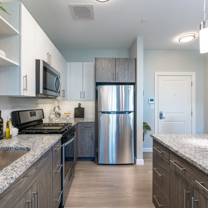 Open kitchen layout with stainless steel refrigerator, granite island, and light wood flooring accents