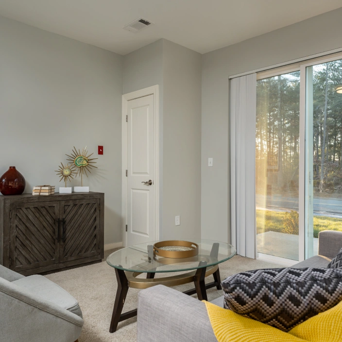 Modern living room with glass coffee table neutral decor and view through sliding glass doors