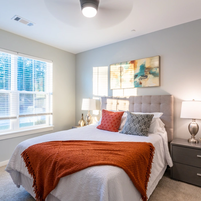 Modern bedroom with white bedding orange throw and abstract wall art illuminated by natural light