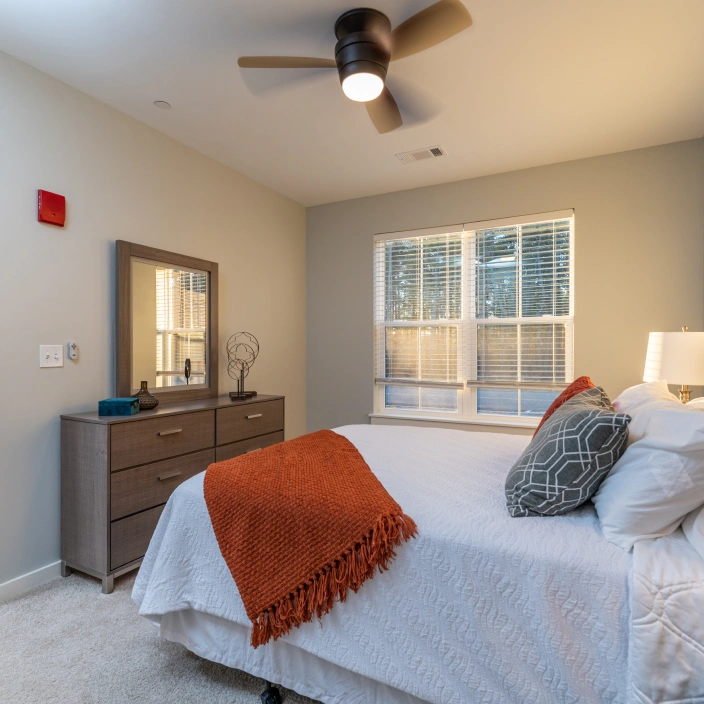 Elegant bedroom design featuring gray dresser mirror and bed with orange throw blanket accents