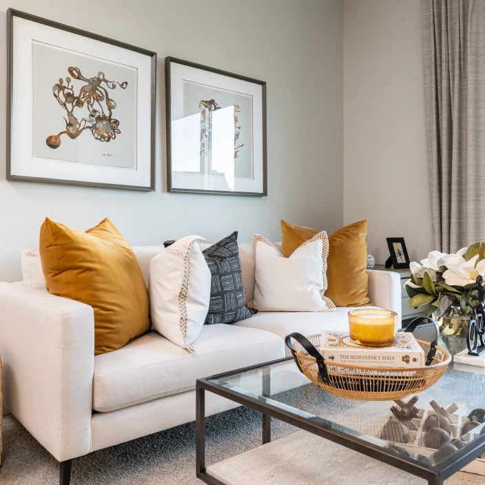 Living room with white sofa, mustard accent pillows, and glass coffee table centerpiece