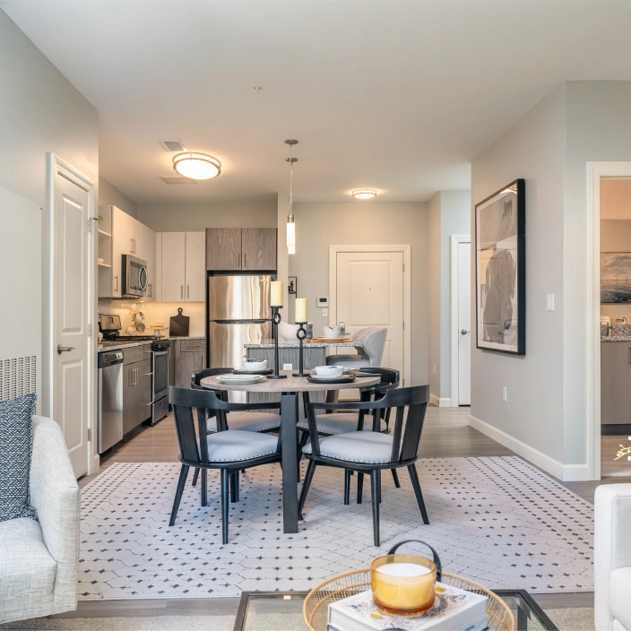 Modern apartment dining area adjacent to open kitchen with stainless steel appliances and granite island
