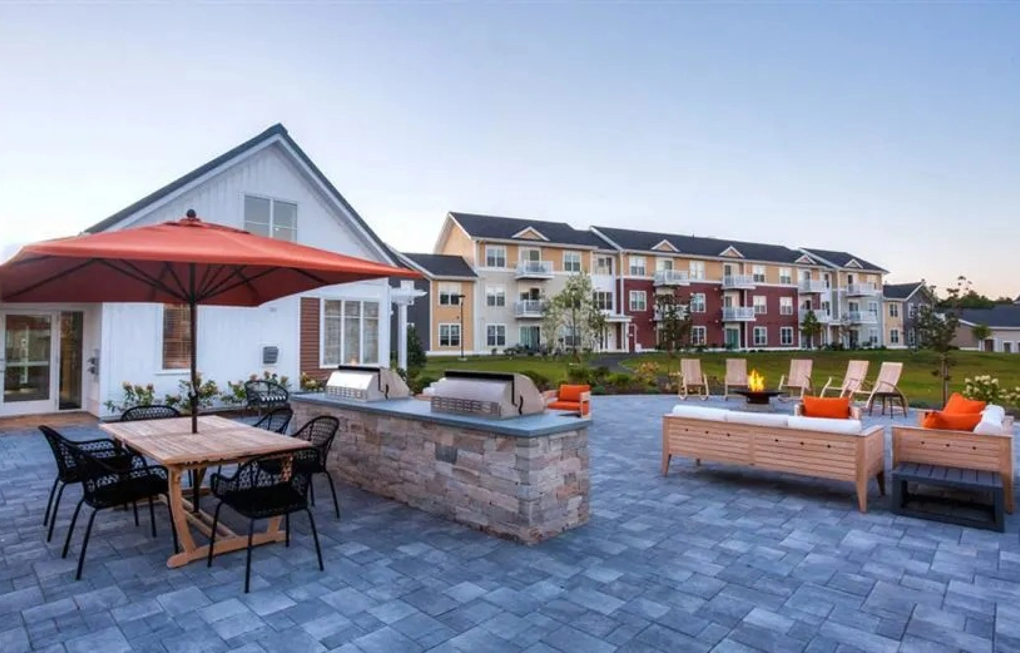 Outdoor community patio with grilling stations, dining table, and cozy fire pit lounge area