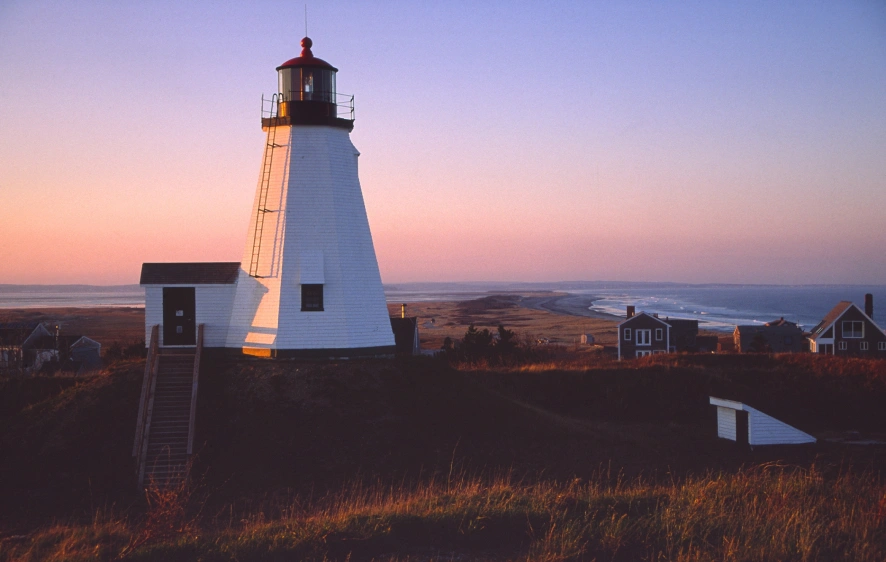White coastal lighthouse overlooking ocean and homes at sunset on peaceful shoreline